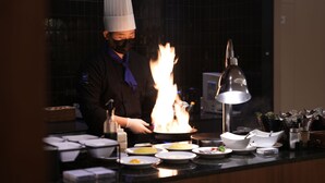 A chef cooking with a flame on a pan in a kitchen. - Eldis Regent Hotel (Daegu)