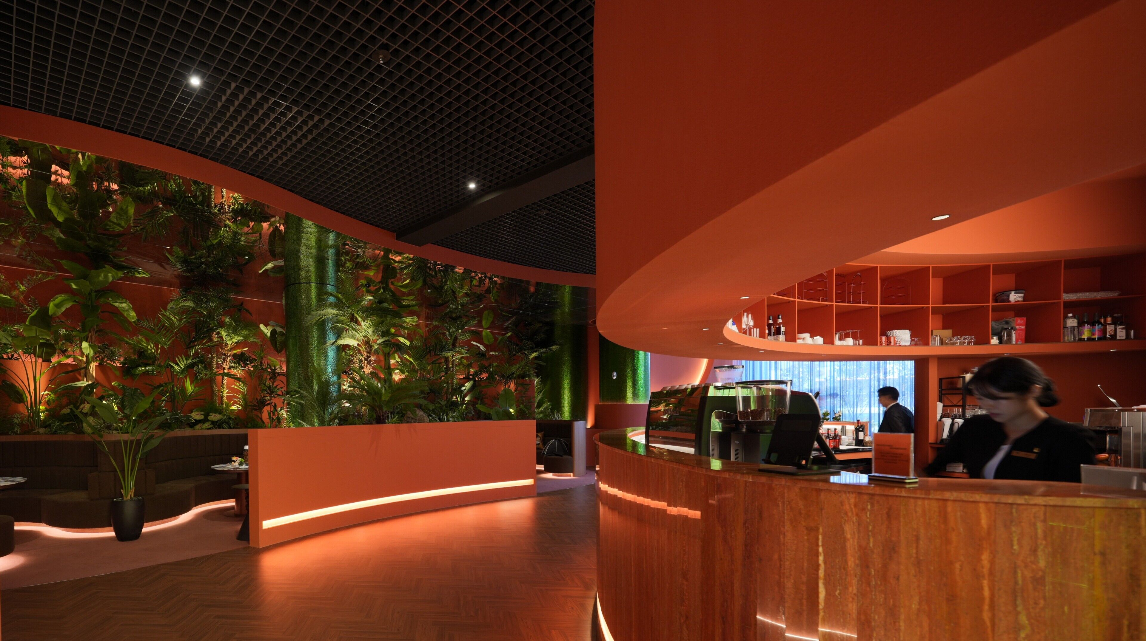 Un interior moderno con mostrador de recepción, zona de bar y una pared cubierta de plantas tropicales.