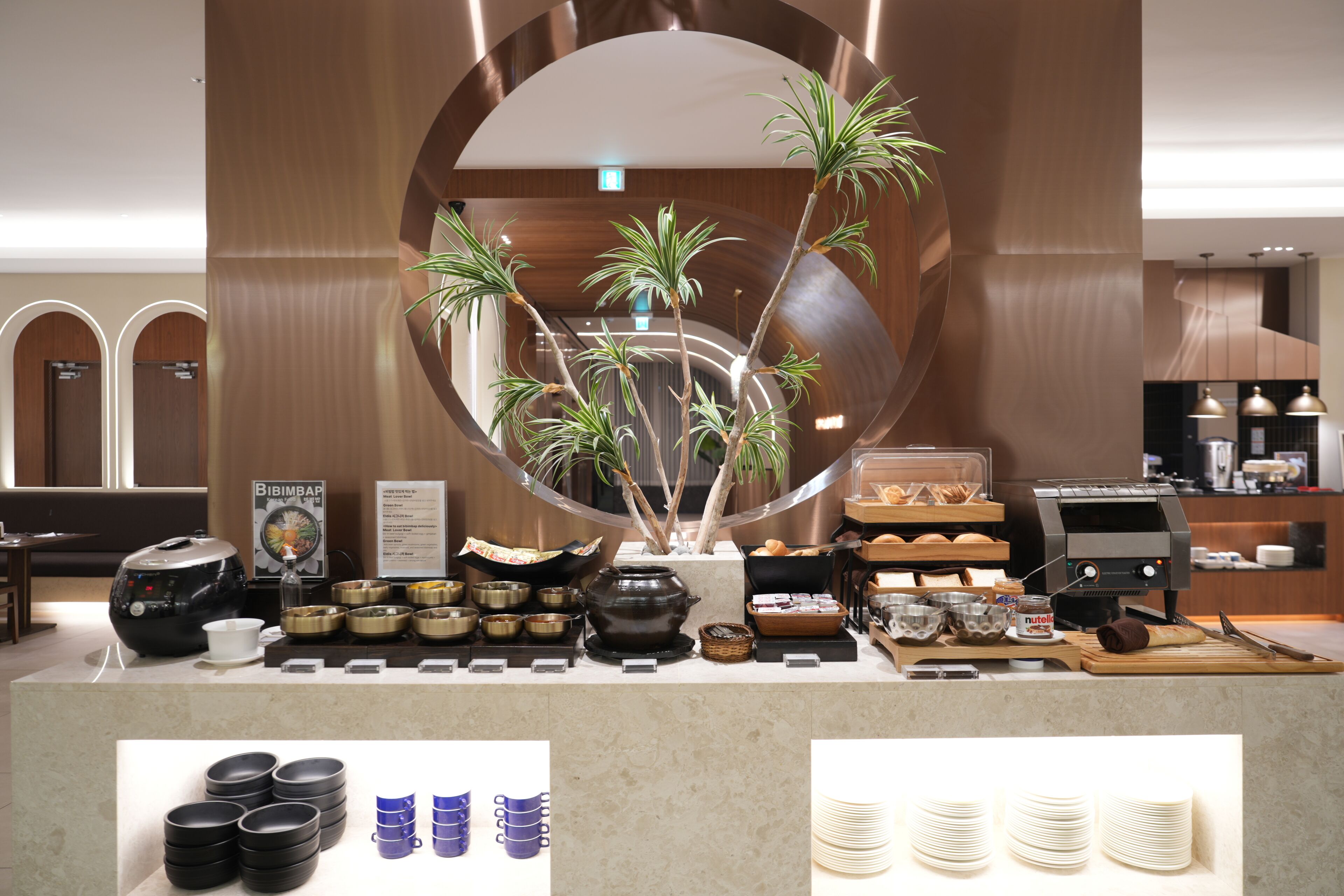 Een buffetgedeelte met diverse voedselcontainers, een koffiemachine en een decoratieve plantenstelling.