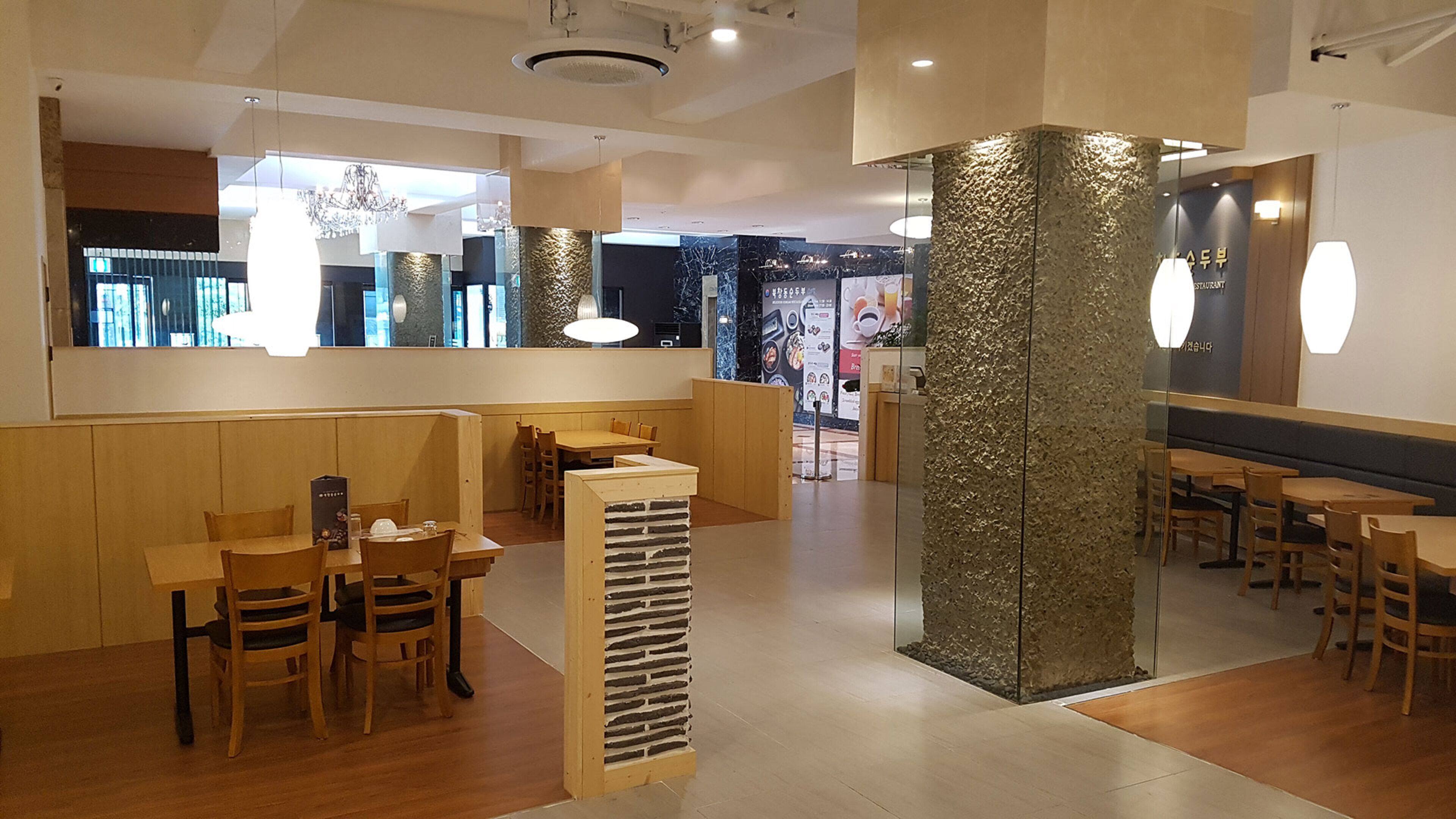 A restaurant interior with wooden tables and chairs, a stone pillar, and a modern chandelier.