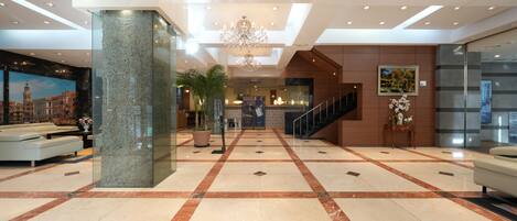 Eine geräumige Lobby mit Marmorboden, einer Rezeption, einer Treppe und einem Chandelier.