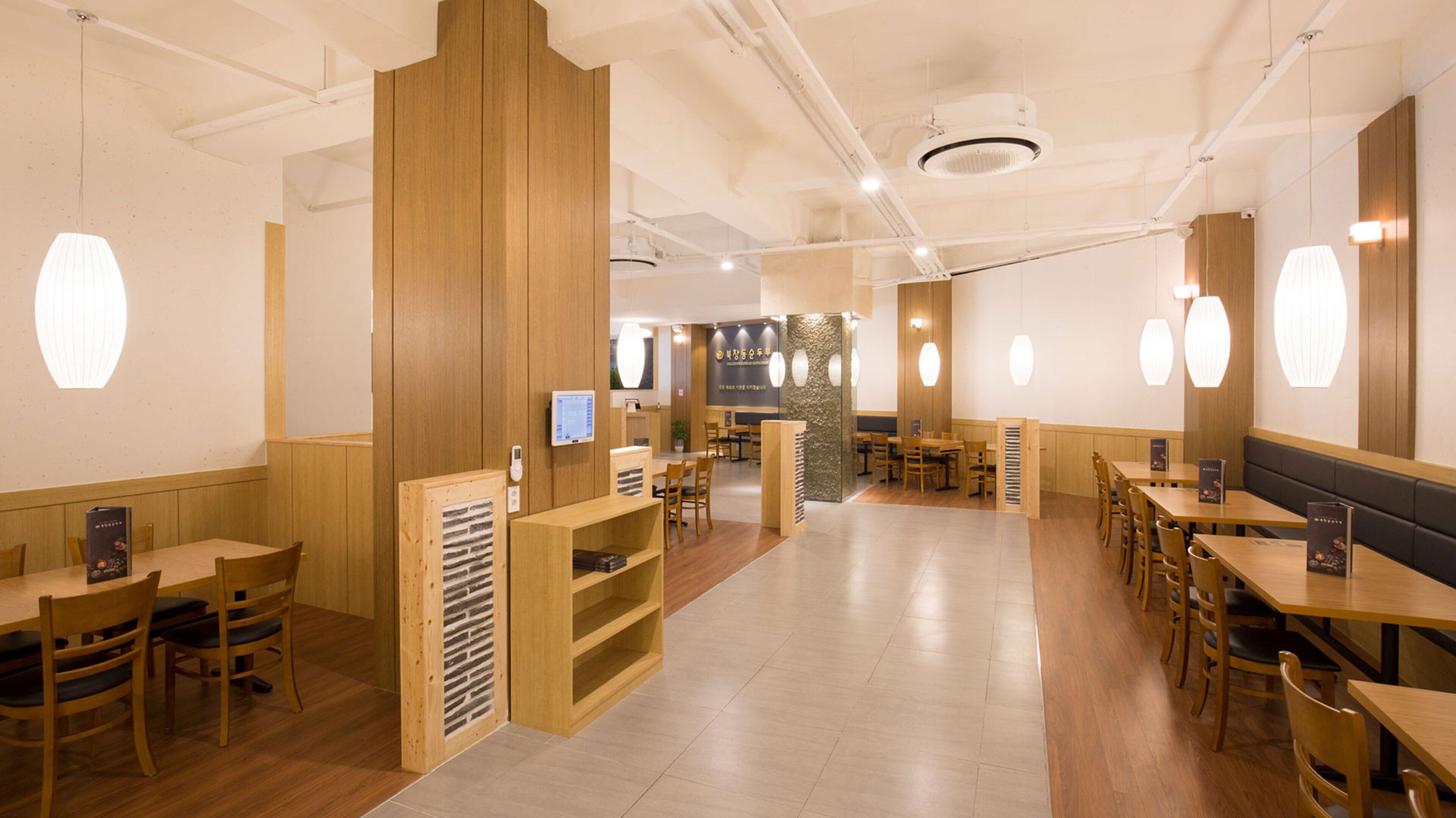 A restaurant interior with wooden tables and chairs, a counter area, and pendant lighting.