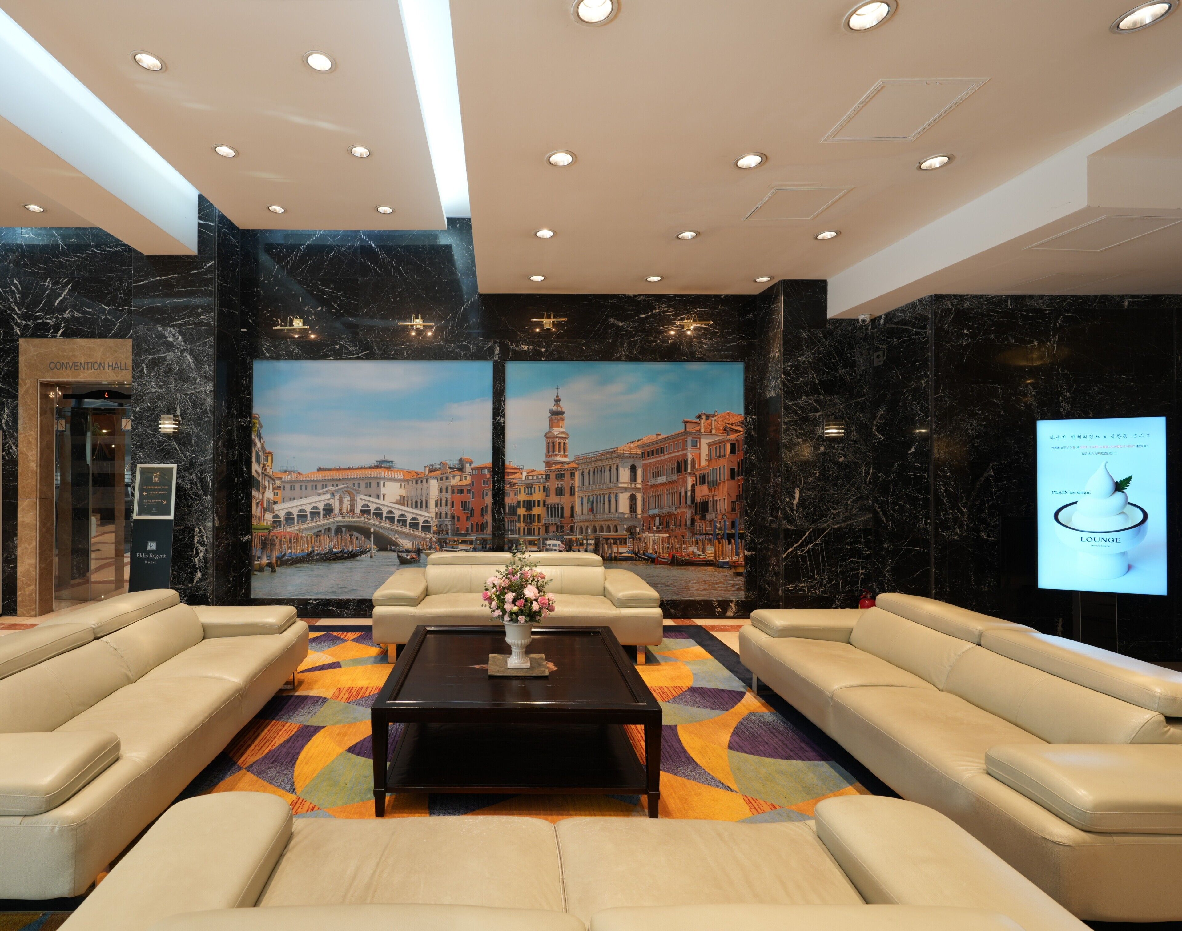 Una hall d'albergo con un grande murale di Venezia, una reception e aree salotto.