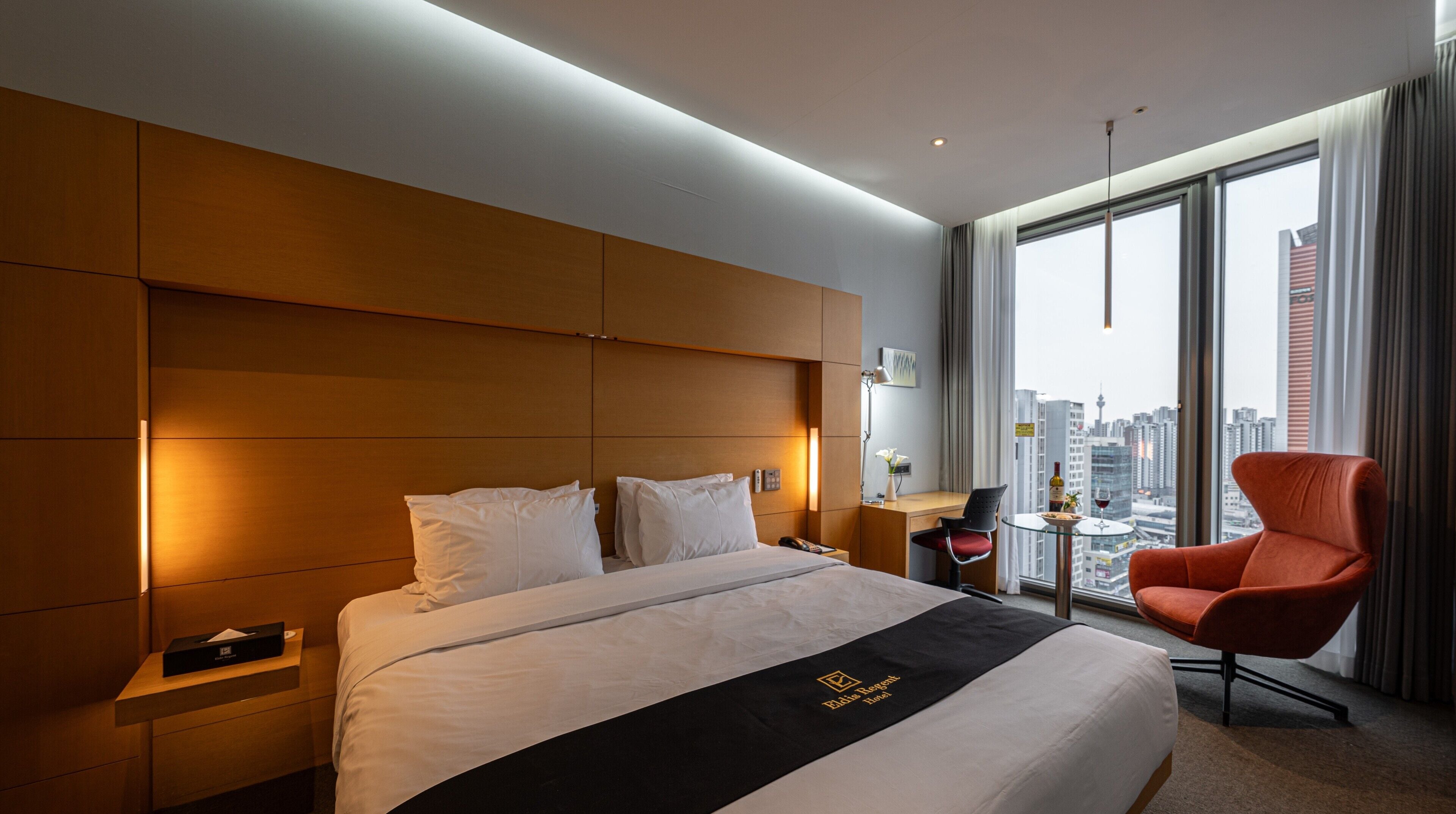 A hotel room with a large bed, a desk, a chair, and a view of the city.