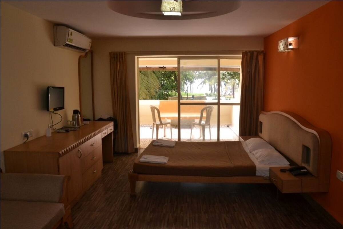 A hotel room with a bed, a desk with a computer, a TV, and a balcony with chairs.