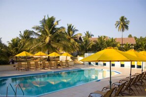A swimming pool with yellow umbrellas and lounge chairs, surrounded by palm trees. - Calangute Residency (Calangute)