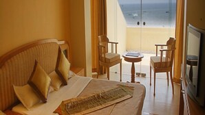 Habitación de hotel con cama, dos sillones, una mesita y televisor. La habitación tiene vista al océano.