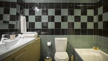 Ein modernes Badezimmer mit einer schwarz-weißen Schachbrettfliesen-Rückwand, einer weißen Toilette, einem Waschbecken mit Spiegel und einer Badewanne.