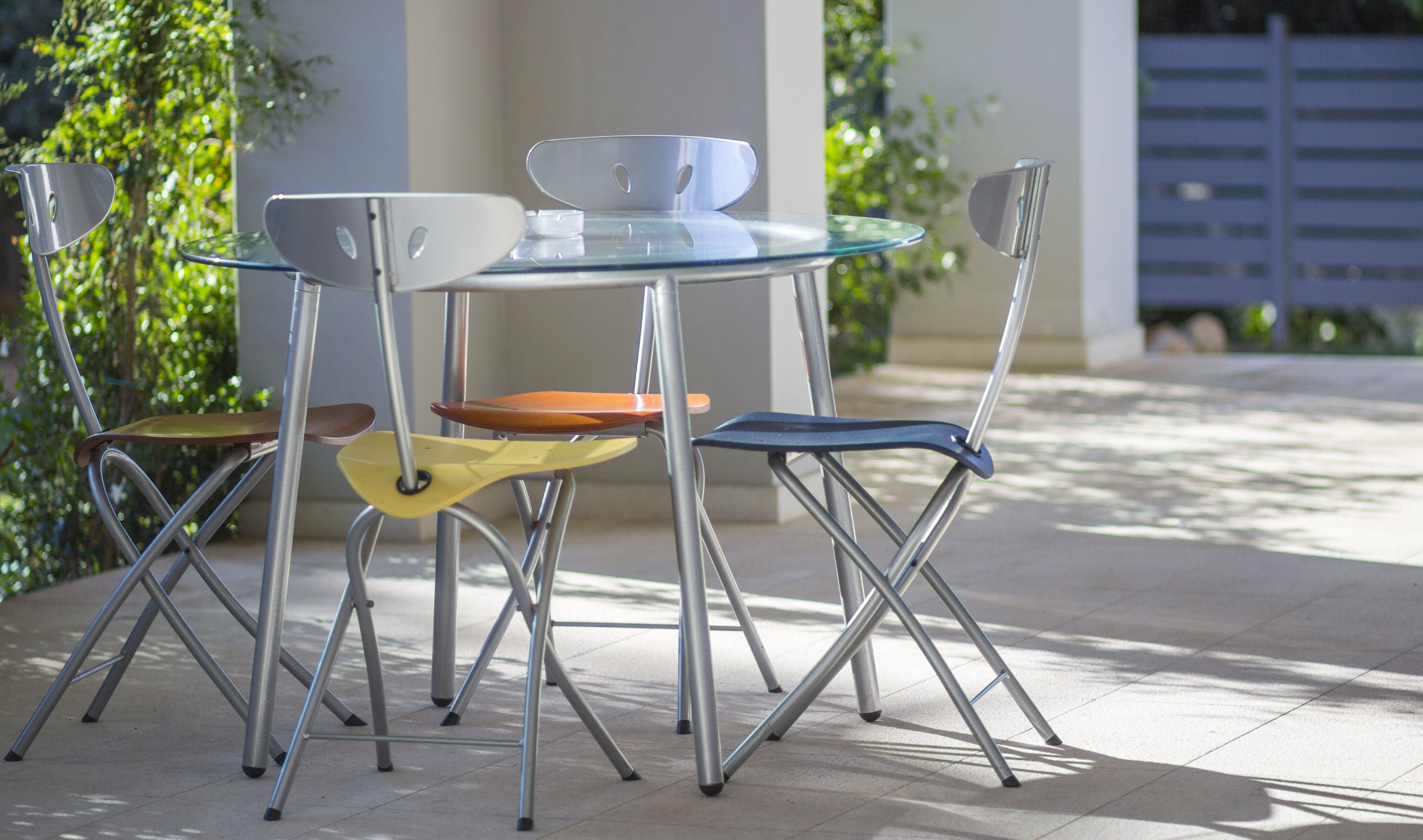 A modern outdoor dining area with a glass table and metal chairs.