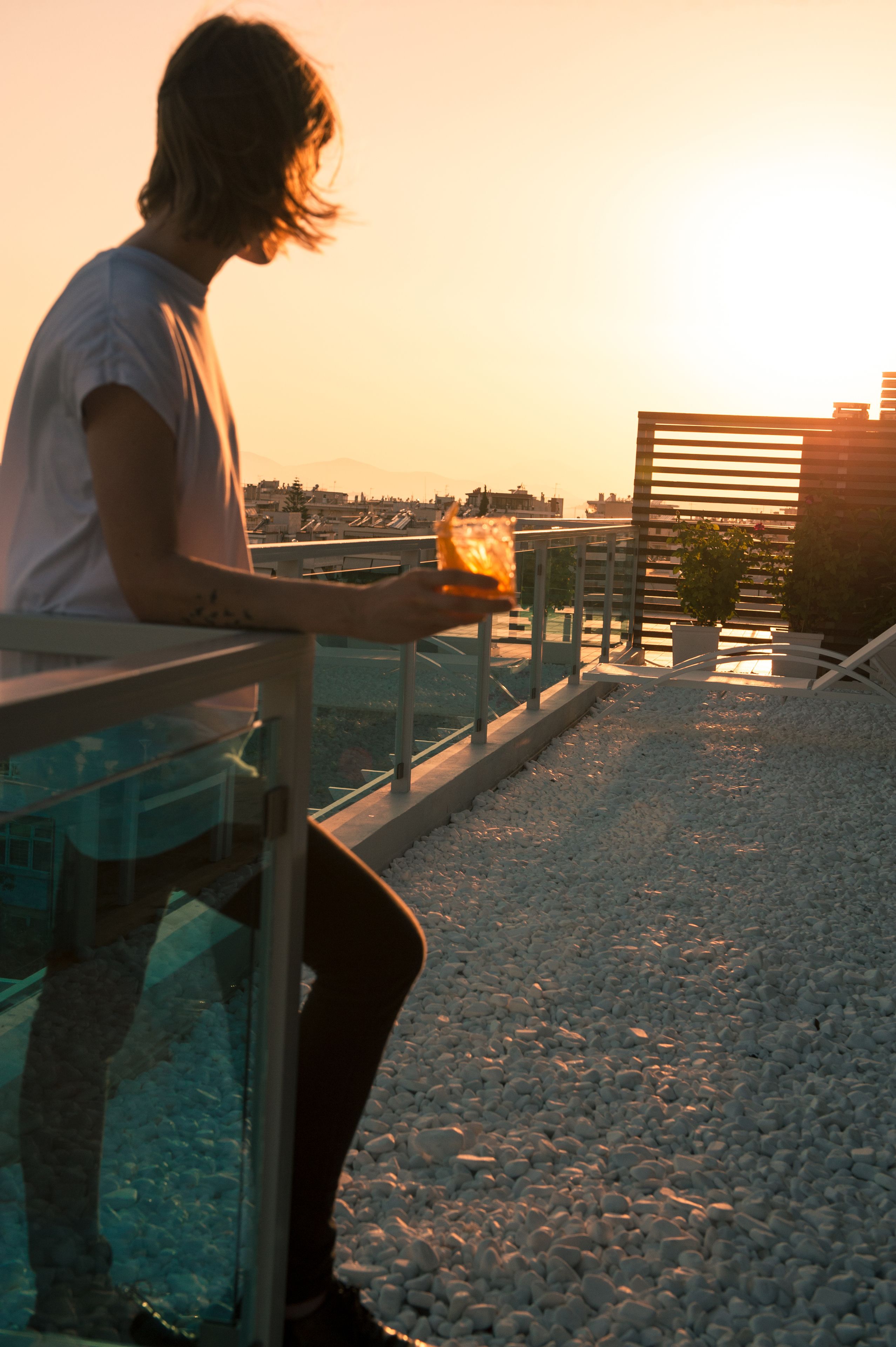 A person sitting on a balcony with a railing, overlooking a cityscape during sunset.