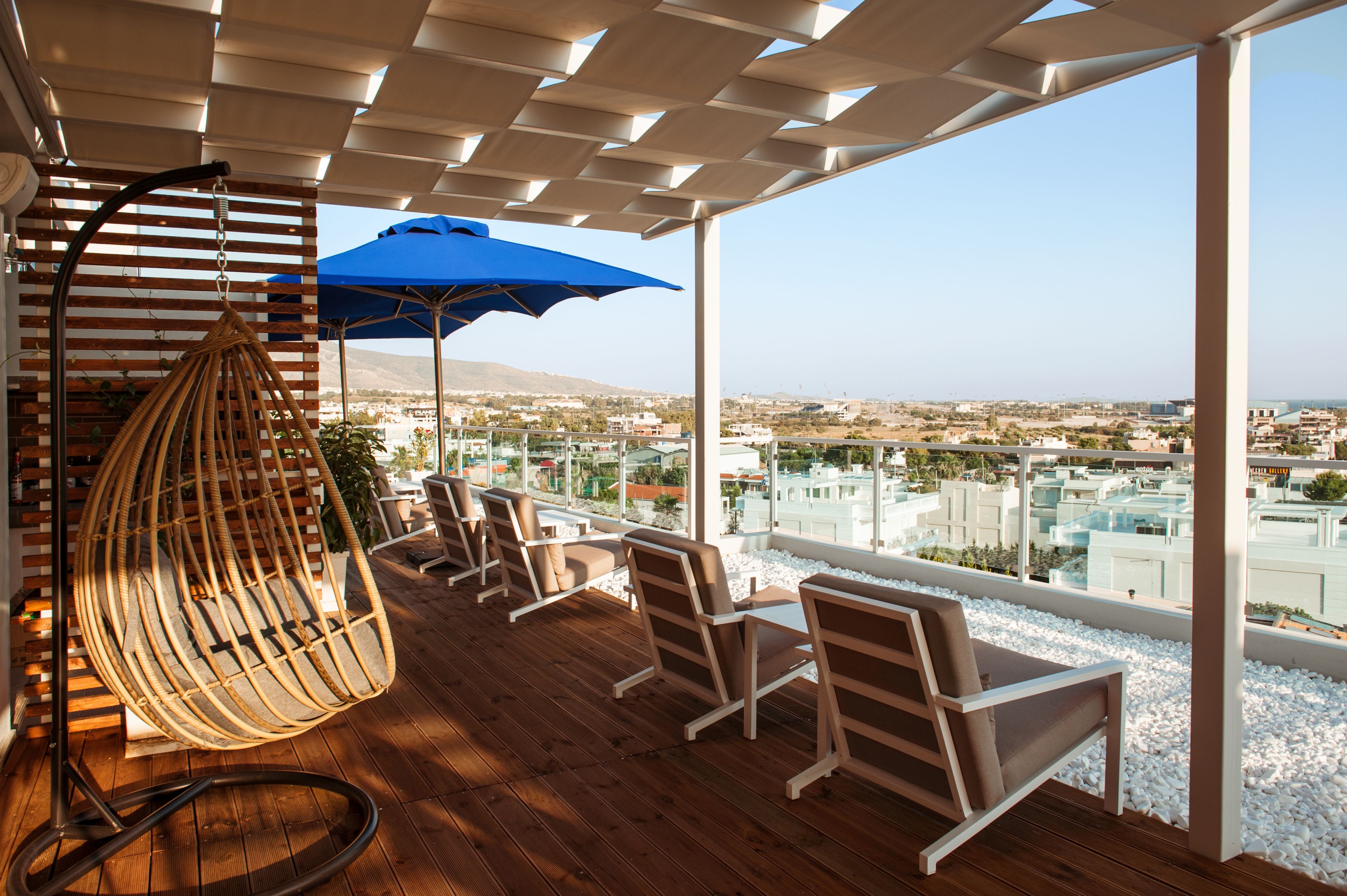 A balcony with wooden flooring, wicker chairs, a blue umbrella, and a hanging chair.