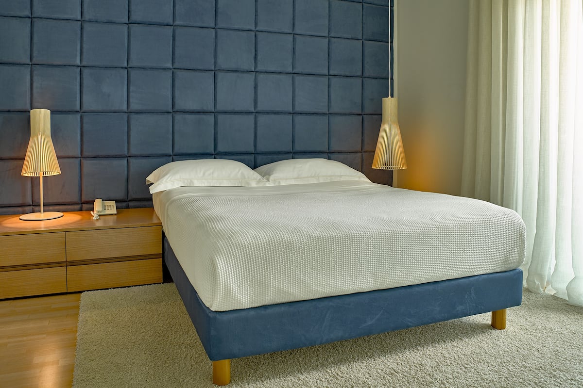 A neatly made bed with a blue headboard, two bedside lamps, and a wooden nightstand with a telephone.