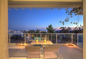 A balcony with a table and chairs, two lanterns, and a view of the cityscape at dusk.