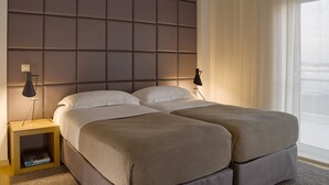 Une chambre d’hôtel moderne avec un grand lit, deux tables de chevet et une grande fenêtre agrémentée de rideaux légers.