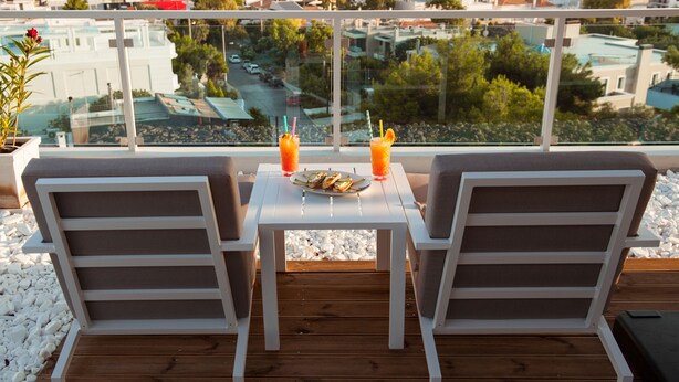 Un balcon avec deux chaises blanches, une petite table et une assiette de nourriture.