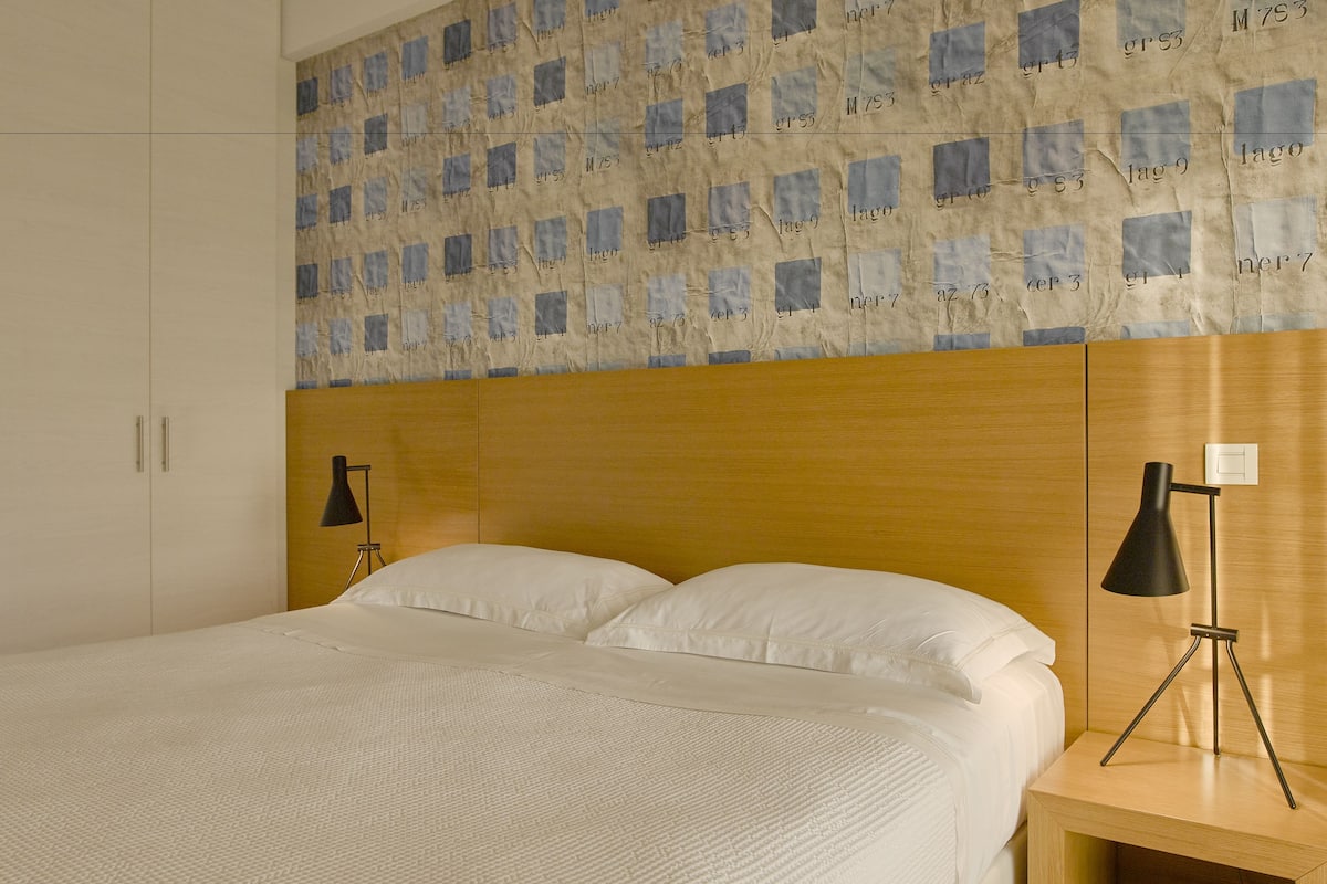 A hotel room with a bed, a wooden headboard, a nightstand with a lamp, and a wardrobe.
