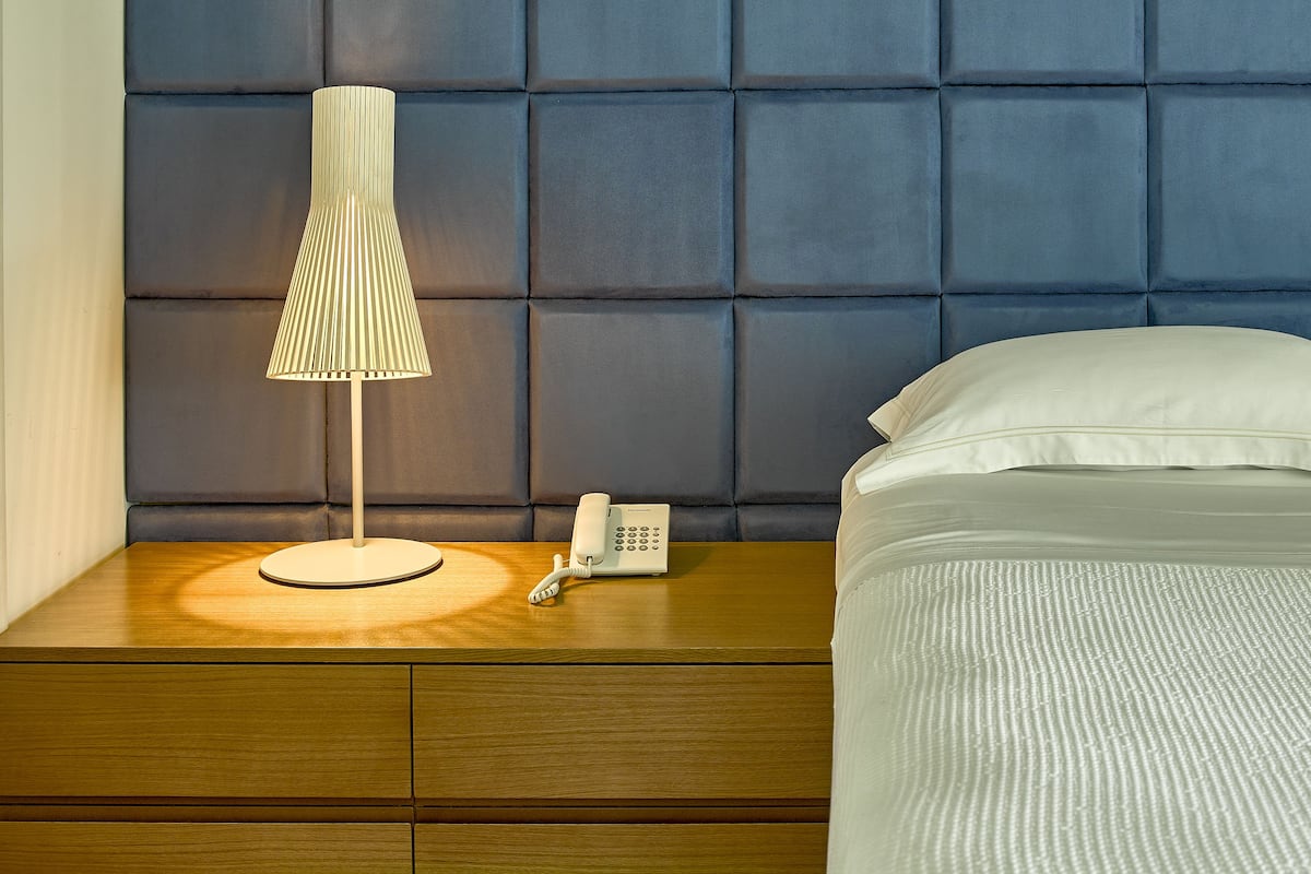 A neatly made bed with white linens, a bedside lamp, and a telephone on a wooden nightstand.