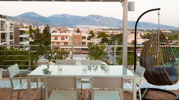 A terrace with a table and chairs, a hanging chair, and a view of a cityscape with mountains in the background.