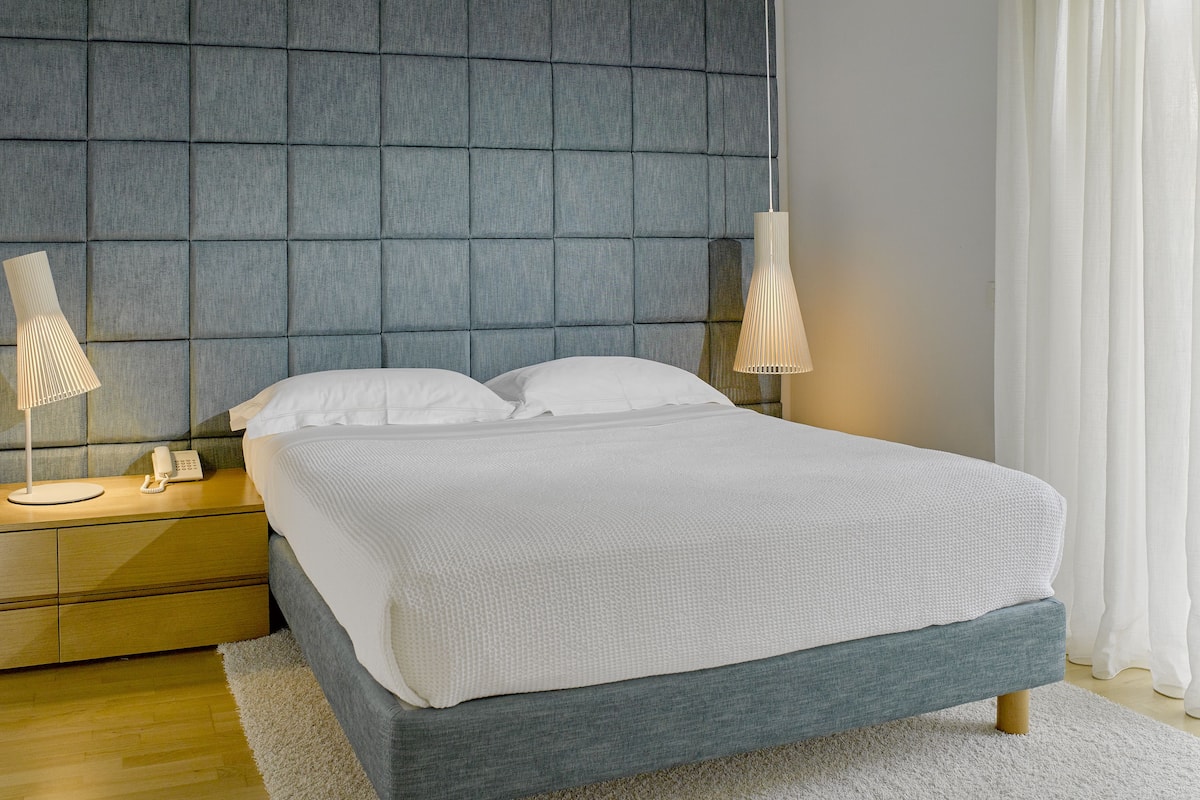 A modern bedroom with a tufted headboard, a large bed with white linens, bedside lamps, and a wooden nightstand.