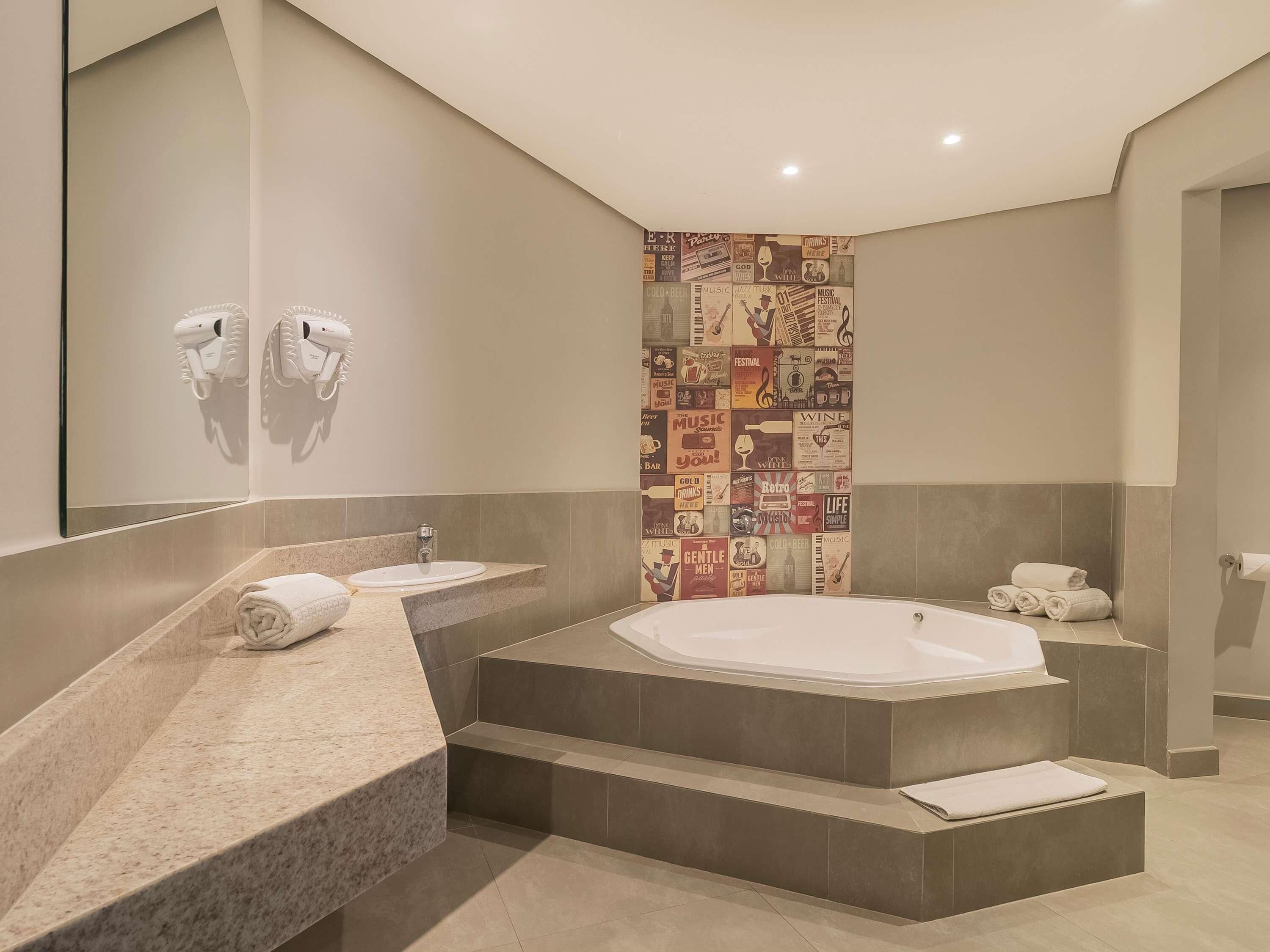 A modern bathroom with a large bathtub, a vanity with a mirror, and a wall decorated with vintage music posters.