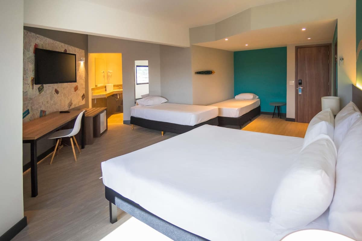 Une chambre d’hôtel avec un grand lit, deux petits lits, un bureau, une chaise, une télévision et une salle de bain.