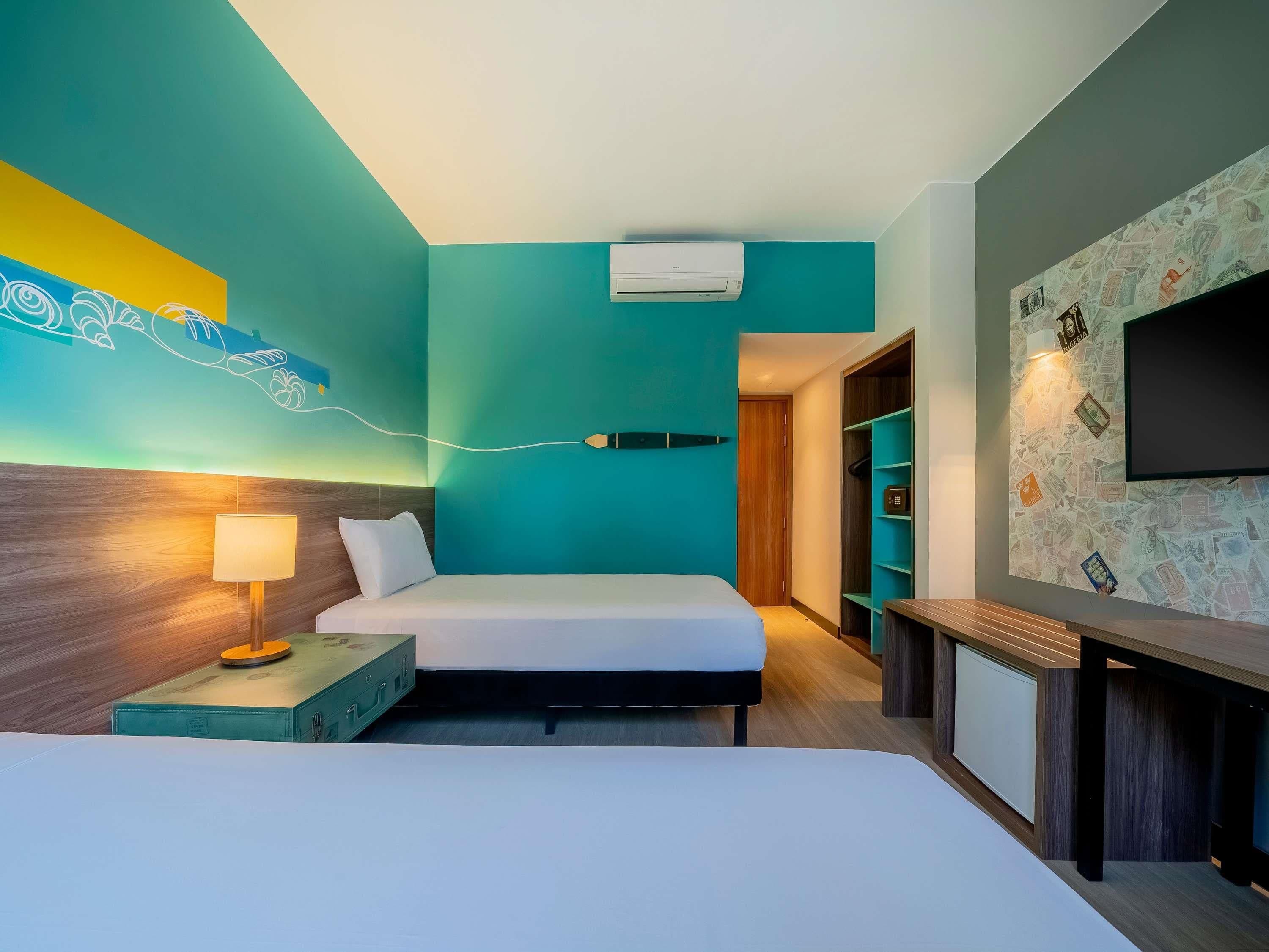 Quarto de hotel com cama, mesa de cabeceira, luminária, ar condicionado, televisão e parede com design de mapa.