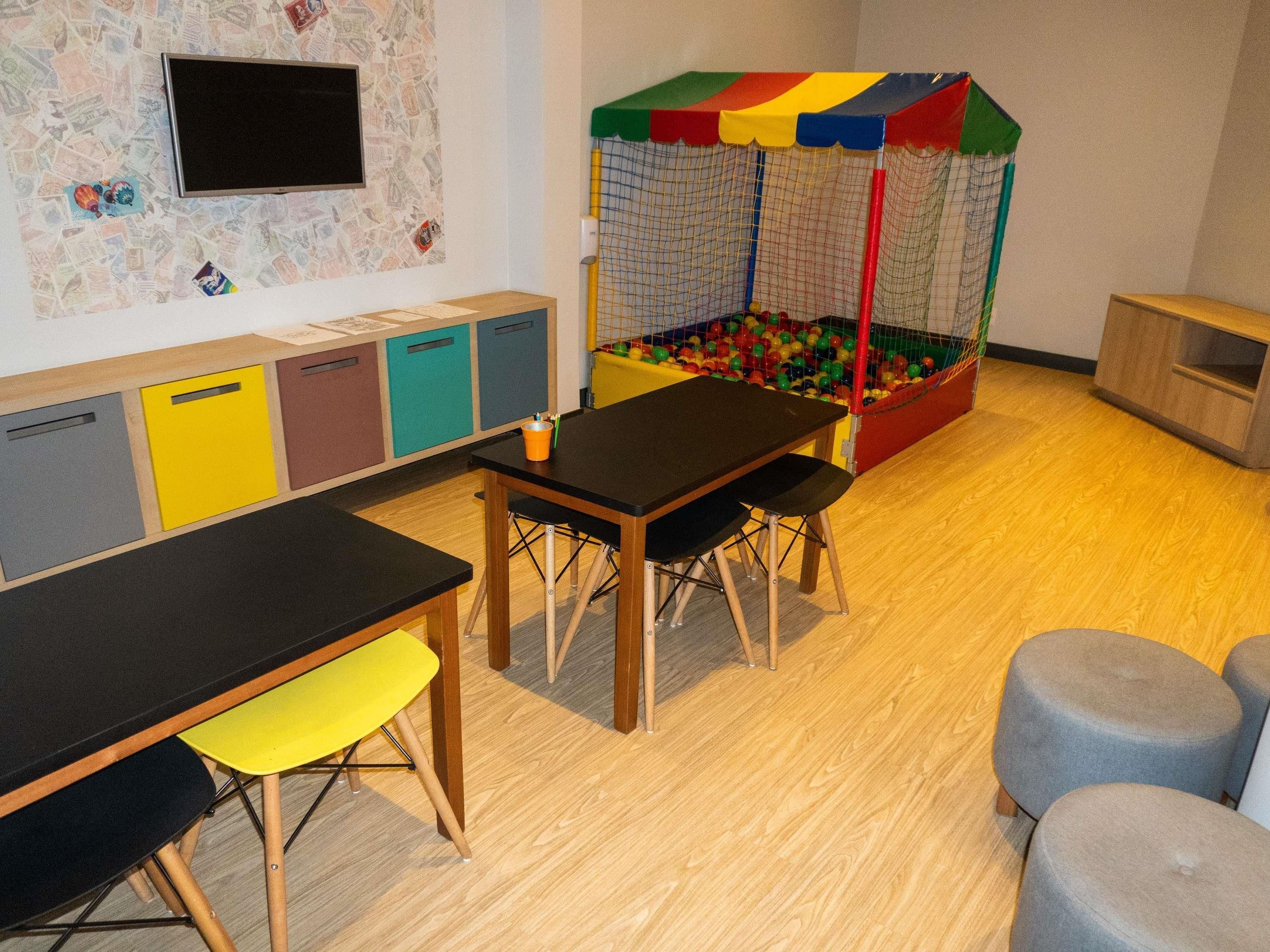 Un área de juegos con piscina de pelotas, una mesa con sillas y un televisor en la pared.