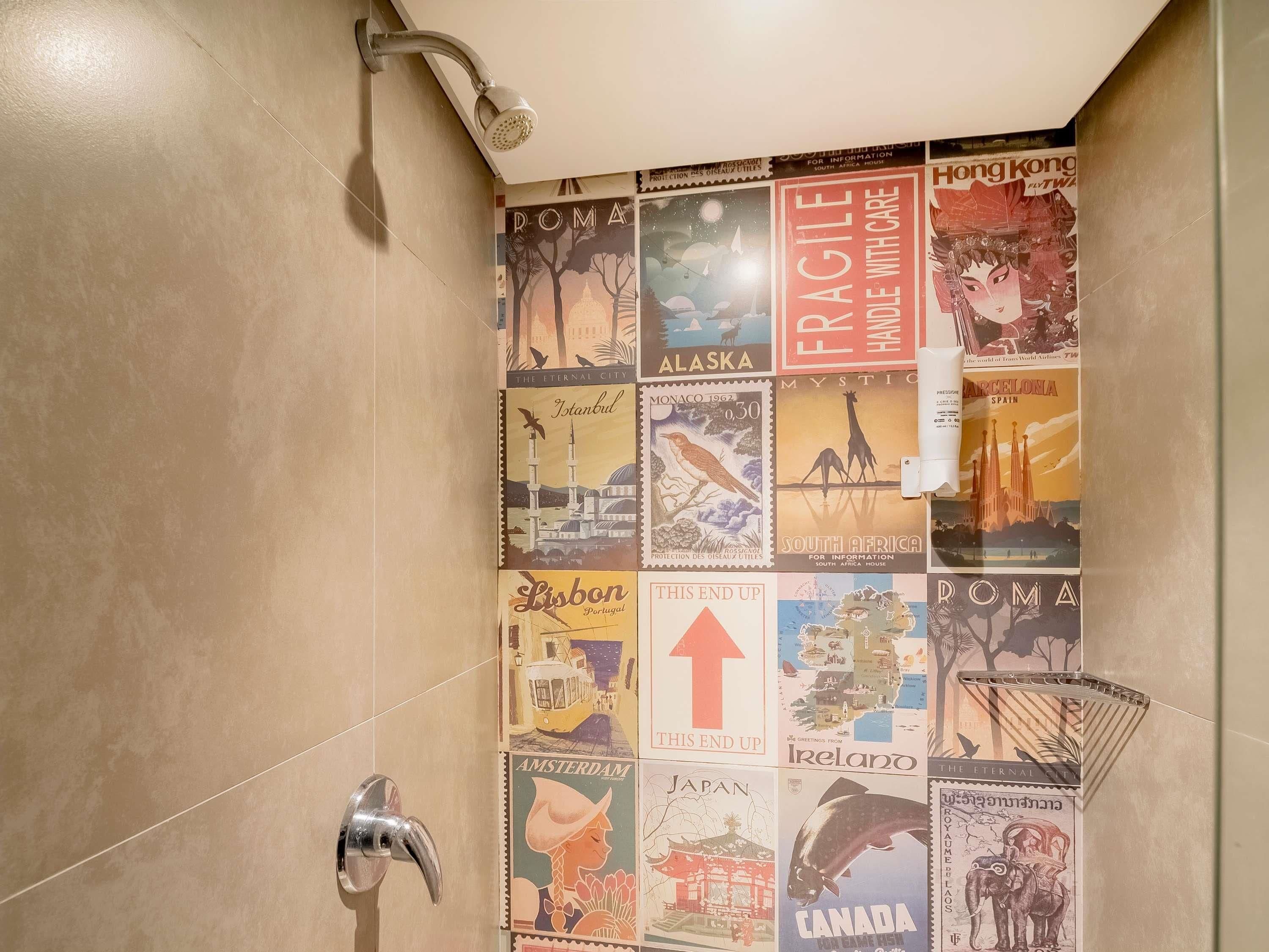 A bathroom with a shower, a wall-mounted towel rack, and a tiled wall with vintage travel posters.