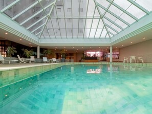 En stor inomhuspool med ett glastak, solstolar och ett träningsområde.