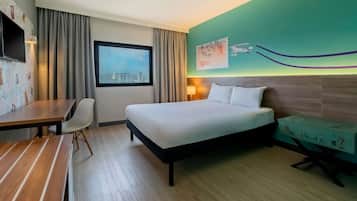 Une chambre d’hôtel avec un lit, un bureau, une chaise, une valise, une fenêtre donnant sur la ville et un mur orné d’une fresque.