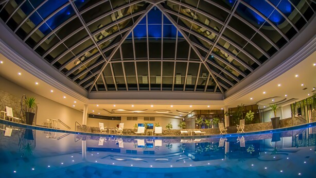 A spacious indoor pool with a glass ceiling, surrounded by lounge chairs and a reception area.
