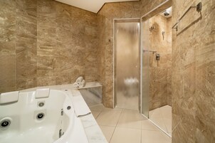 Un baño moderno con pared de mármol, ducha con cerramiento de vidrio y una bañera grande.