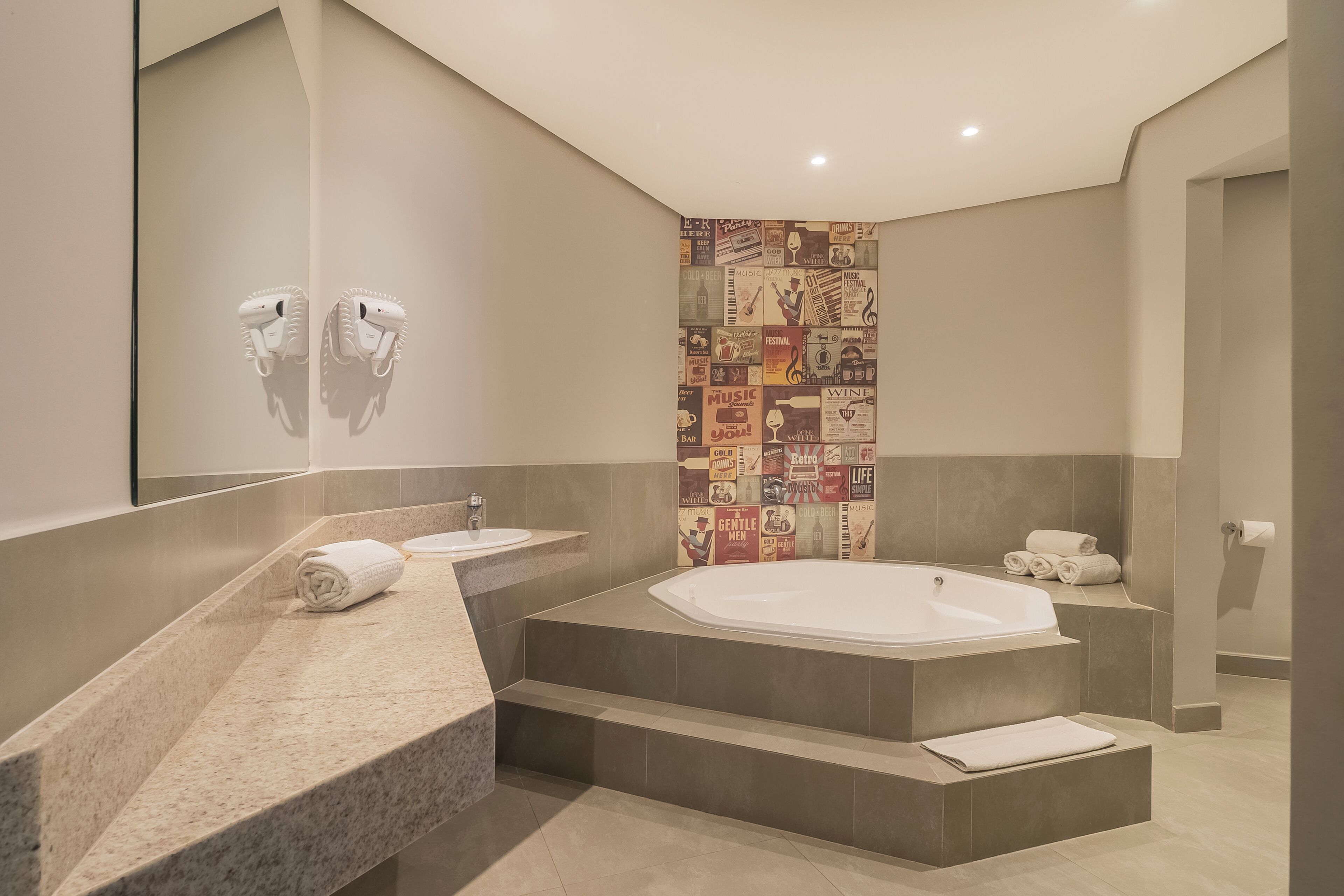 A modern bathroom with a large bathtub, two sinks, and a tiled wall with various posters.