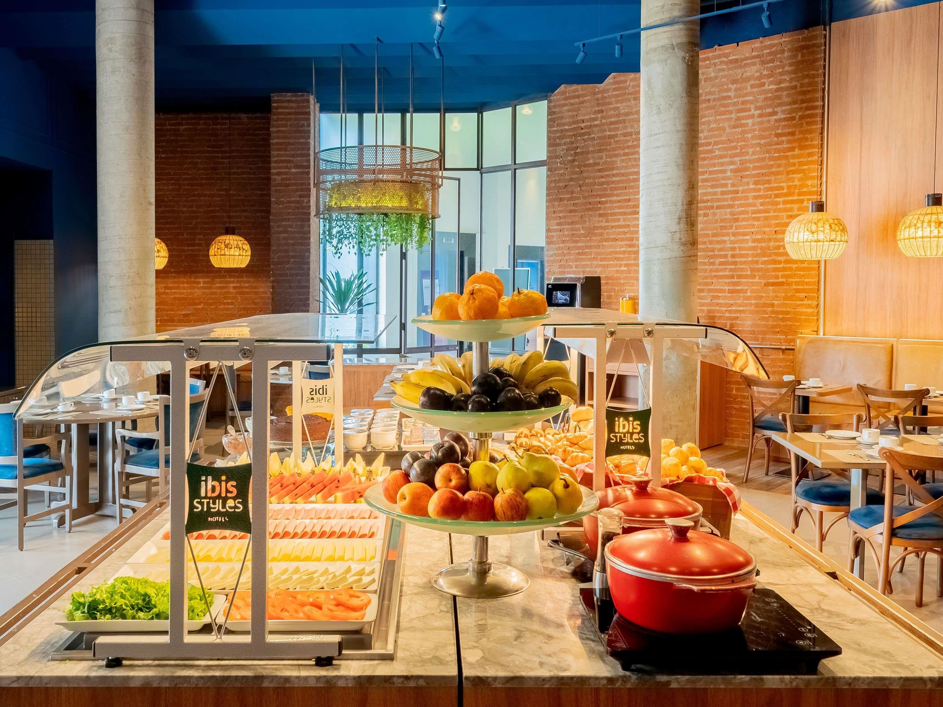 Un bufé con diversas frutas y verduras, una vitrina de vidrio y una olla roja sobre el mostrador.