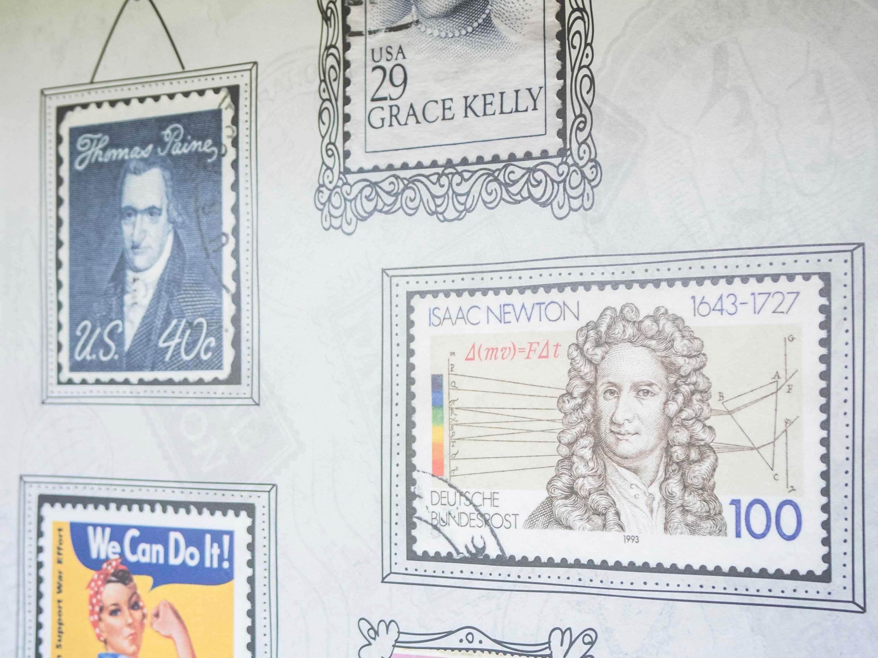 Una pared con varios sellos postales, incluyendo un sello de 40 centavos de Thomas Paine, un sello de 29 centavos de Grace Kelly, un sello de 100 centavos de Isaac Newton, y un cartel que dice 'We Can Do It!'.