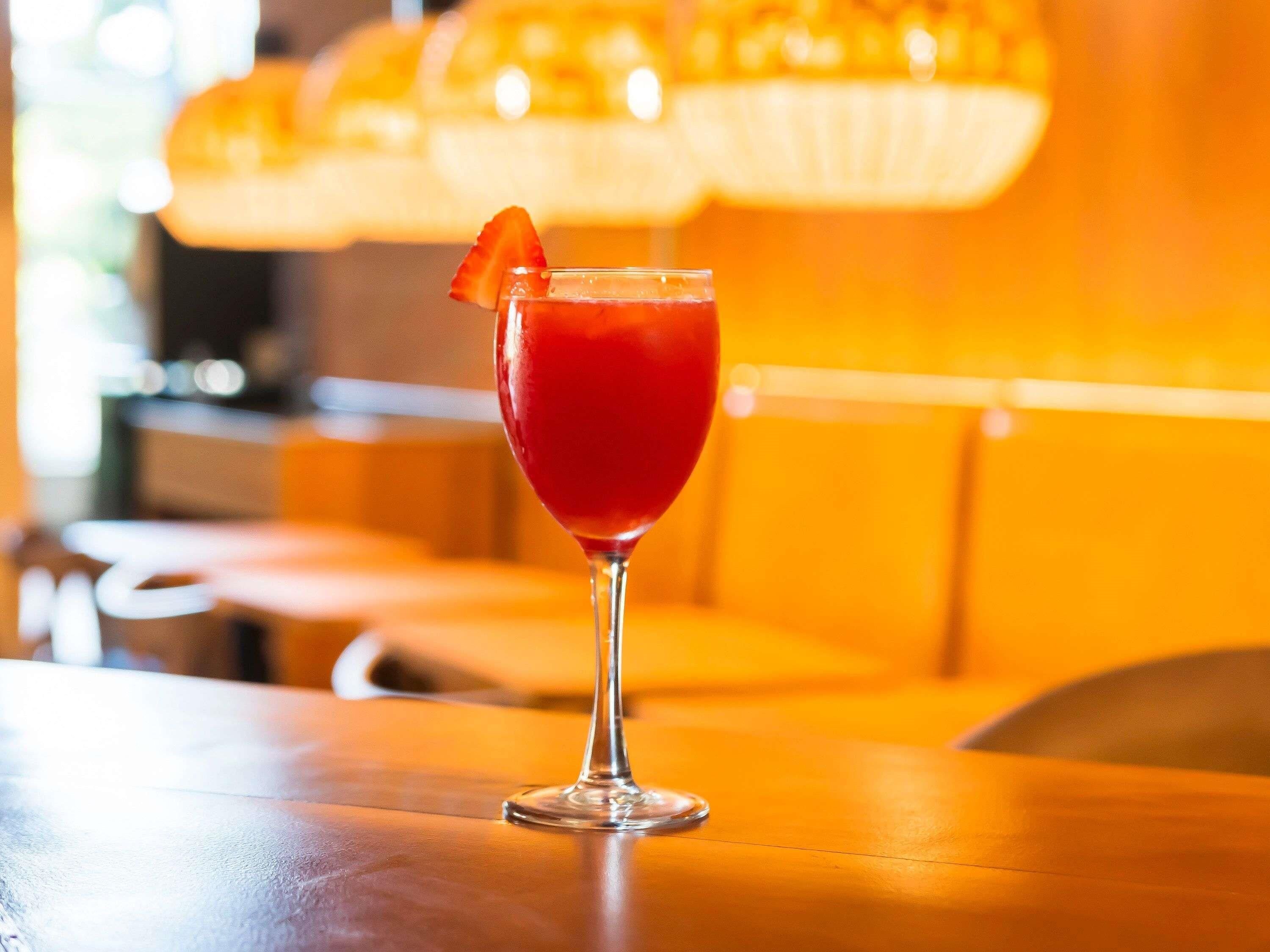 A glass of red beverage with a garnish on a table in a warmly lit indoor setting.