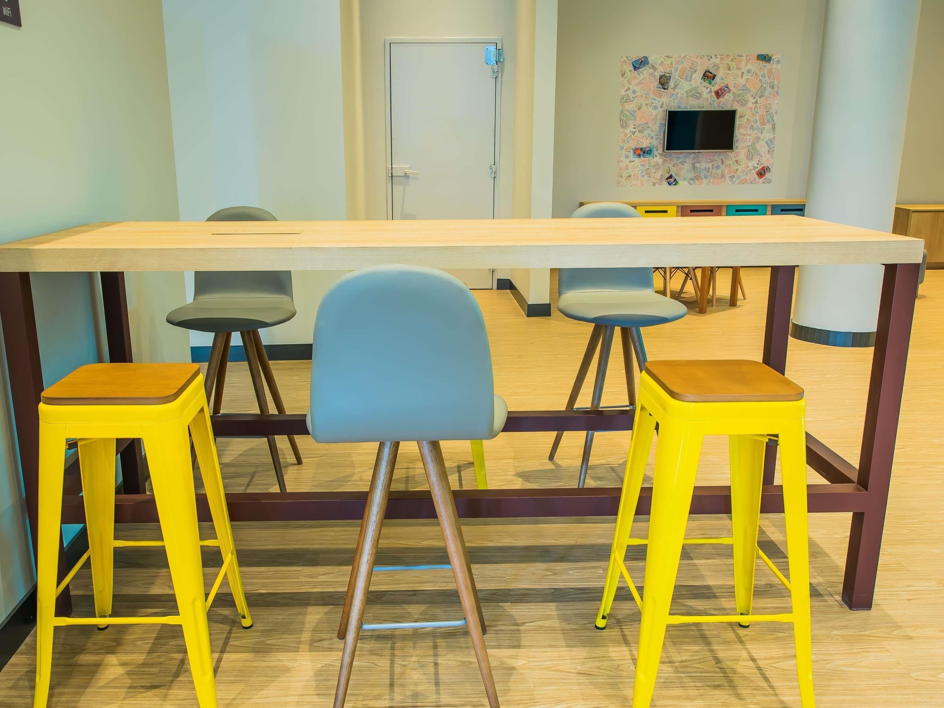 A conference room with a long table, four chairs, and two yellow stools.