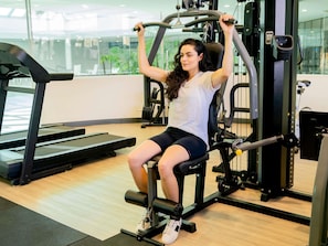 A person using a leg press machine in a gym with a treadmill and weights in the background.