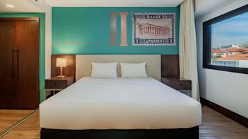 Una habitación de hotel con una cama grande, dos mesitas de noche, aire acondicionado de pared y ventana con vistas a la ciudad.