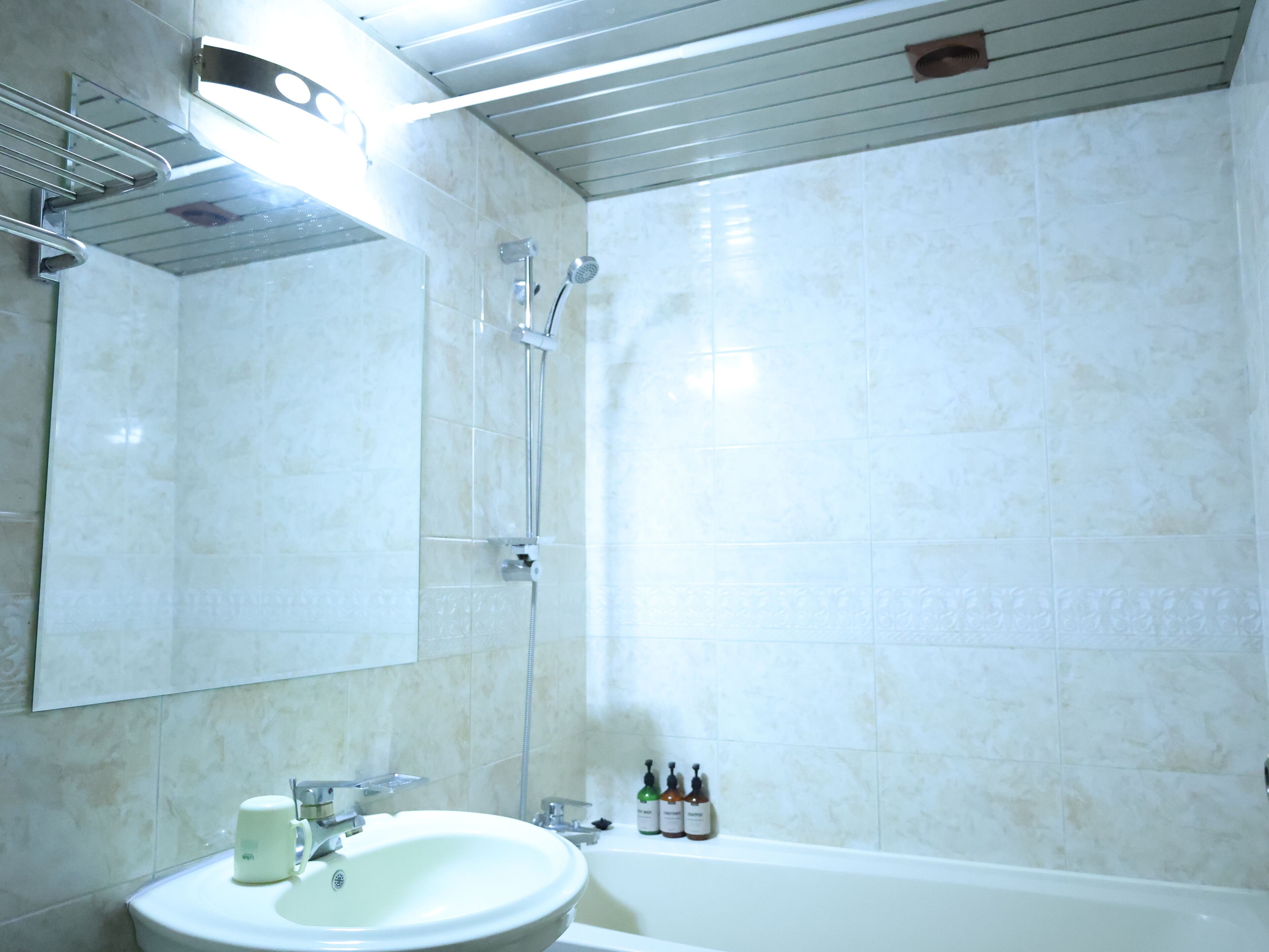 A bathroom with a sink, mirror, shower, and three bottles of toiletries.