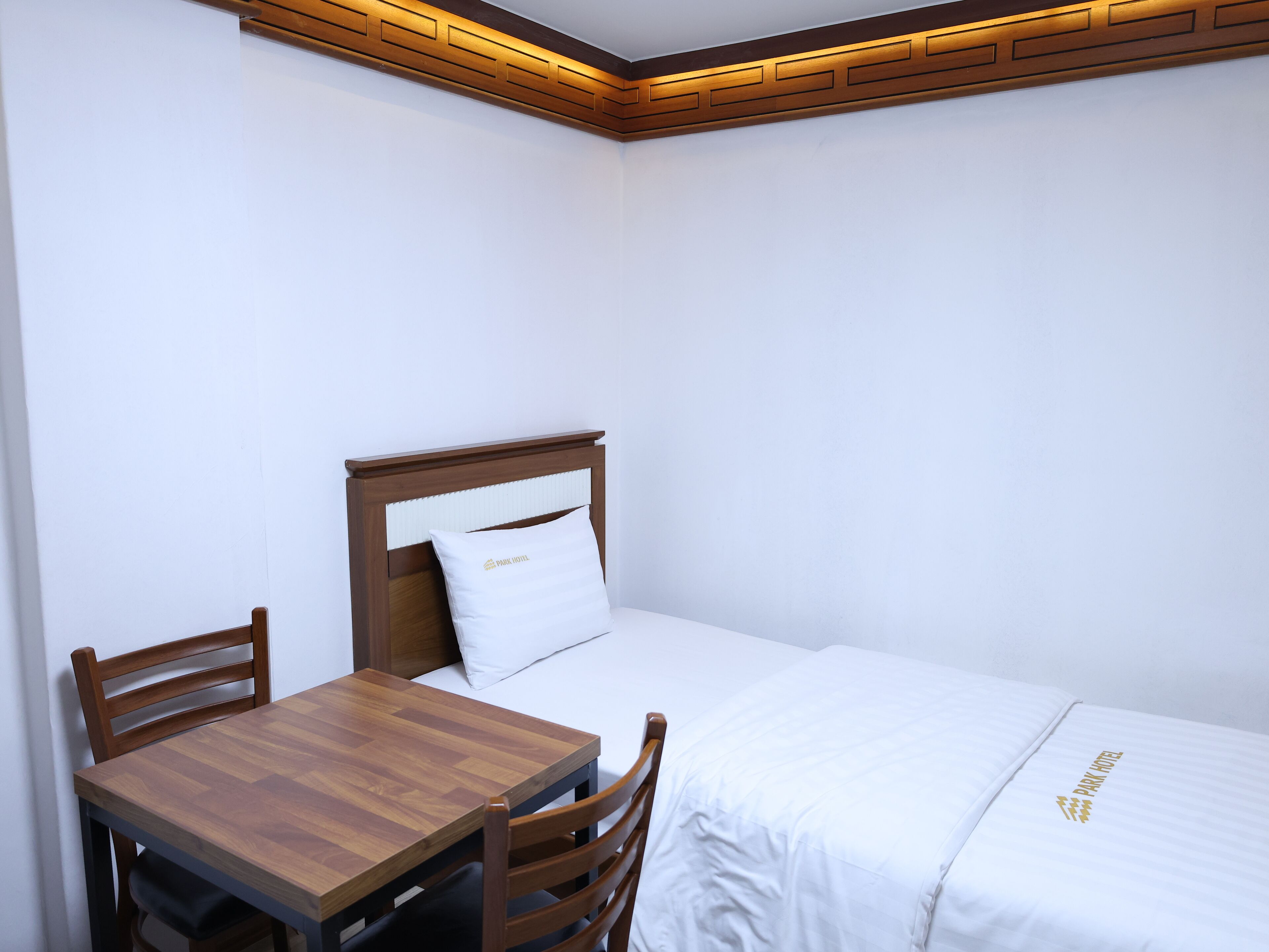 Ein kleines, aufgeräumtes Schlafzimmer mit einem hölzernen Bett, einem passenden Nachttisch und zwei Stühlen.