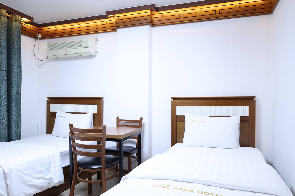 Een hotelkamer met twee eenpersoonsbedden, een houten tafel en een stoel.