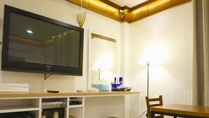 Une chambre d’hôtel équipée d’une télévision, d’un bureau avec une lampe, d’une chaise et d’une petite kitchenette.