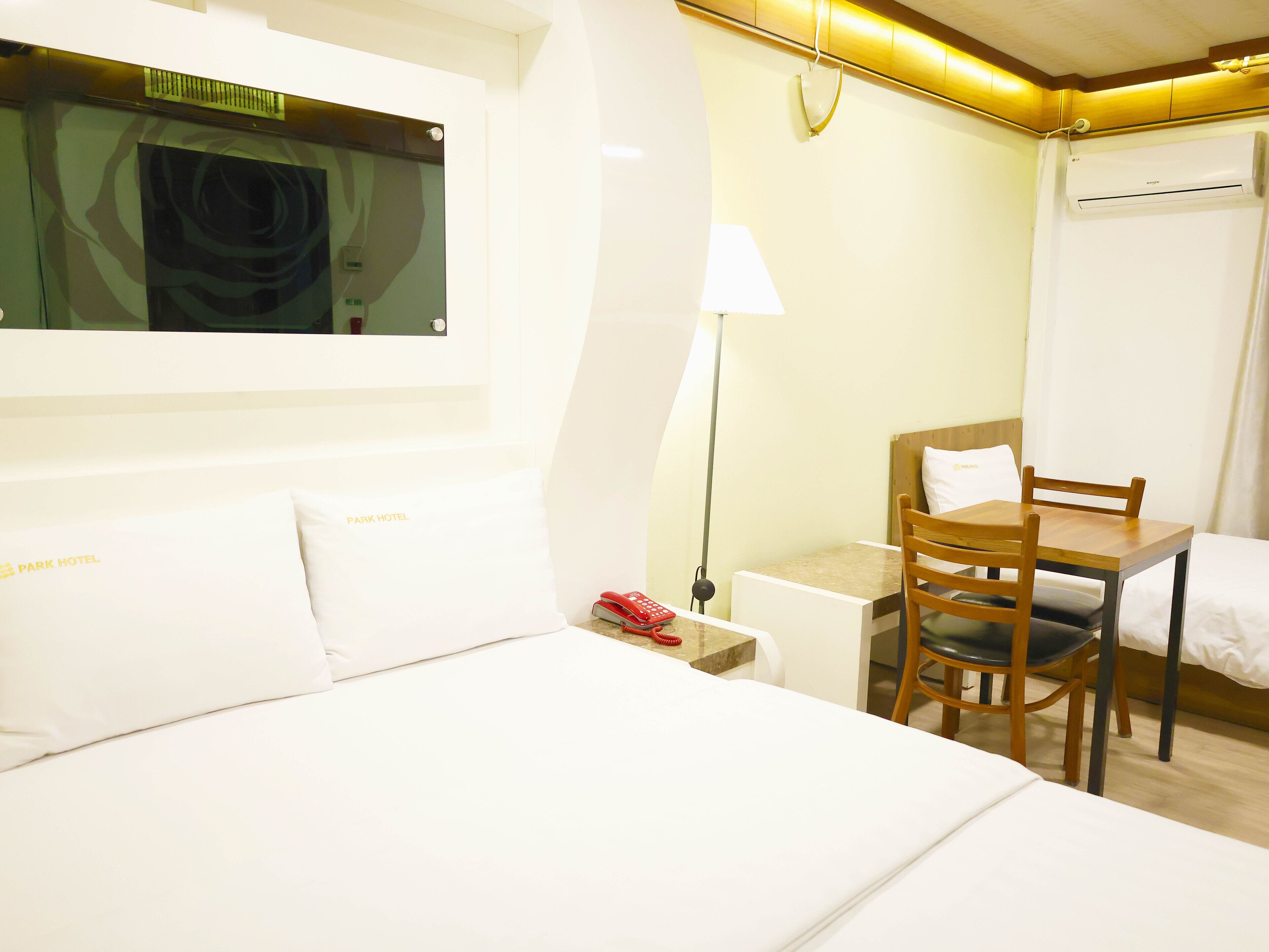 Una habitación de hotel con cama, escritorio, silla, lámpara y ventana con cortinas.