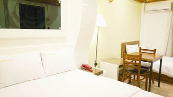 Una habitación de hotel con cama, escritorio, silla, lámpara y ventana con cortinas.