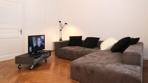 A living room with a sectional sofa, a TV on a cart, and a lamp. - Apartments Spalenring10 (Basel)