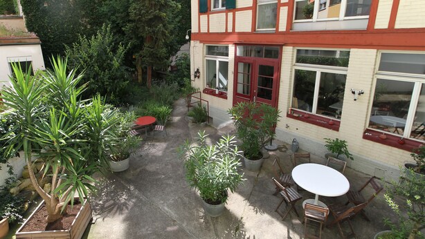 A courtyard with a wooden table and chairs, surrounded by potted plants and a building with red-framed windows. - Apartments Spalenring10 (Basel)