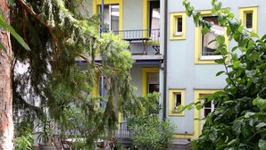 A courtyard with dense greenery, a tree, and a building with yellow windows and balconies. - Apartments Spalenring10 (Basel)