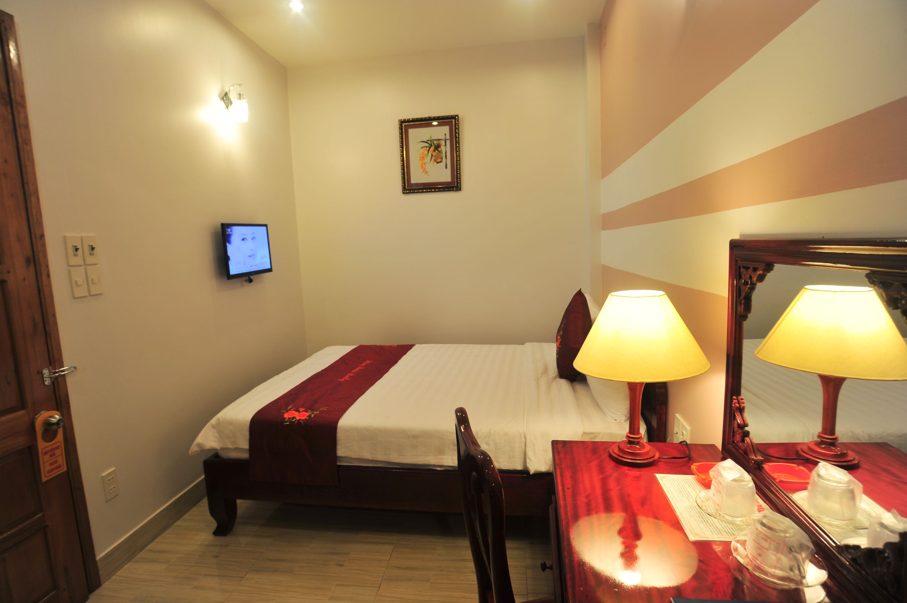 A hotel room with a bed, bedside lamps, a television, and a mirror.