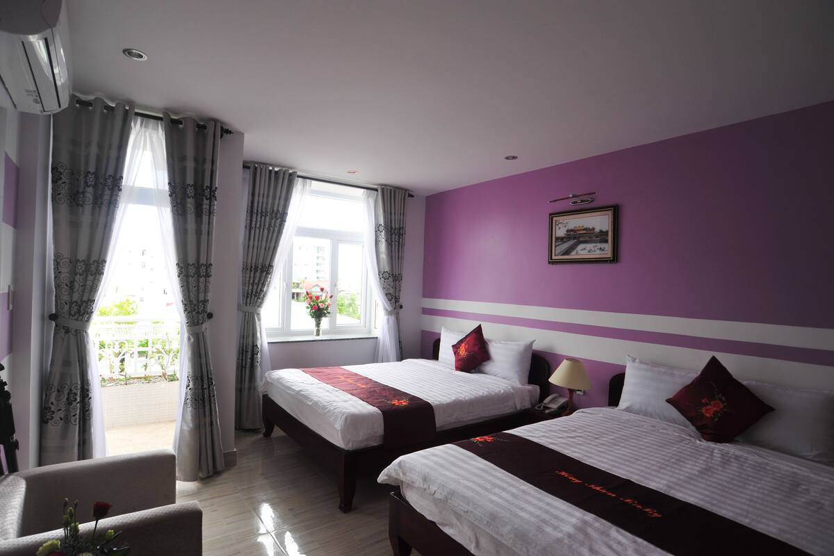 Habitación de hotel con dos camas, una ventana con cortinas, una silla y un cuadro en la pared.